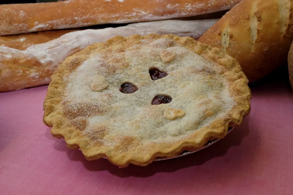 A pie with four spots on it sitting next to some bread.