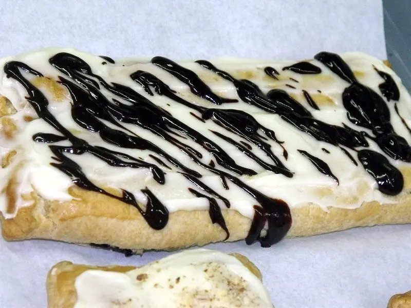 A piece of bread with white icing and chocolate sauce.